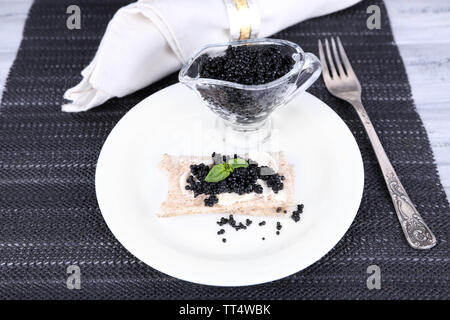 Fetta di pane con burro e caviale nero sulla piastra sul tovagliolo su sfondo di legno Foto Stock