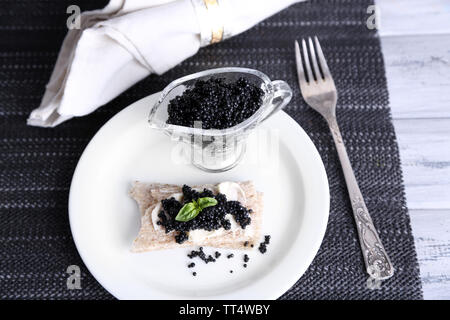 Fetta di pane con burro e caviale nero sulla piastra sul tovagliolo su sfondo di legno Foto Stock