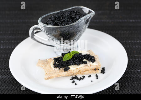 Fetta di pane con burro e sauceboat con caviale sulla piastra sul tessuto scuro dello sfondo Foto Stock