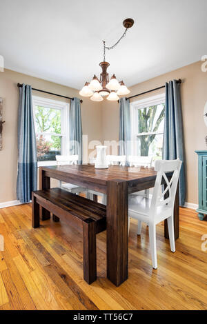 Un marrone tavolo da pranzo con un lampadario appeso al soffitto in legno chiaro pavimenti colorati. Foto Stock