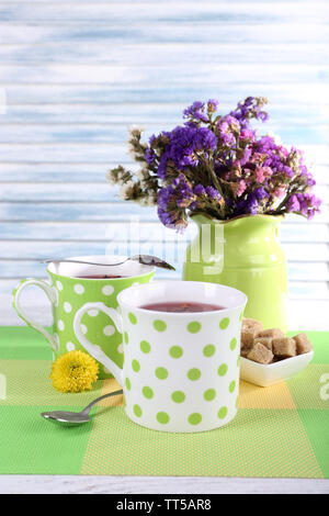 Due polka dot tazze con zucchero e fiori di campo in vaso sulla tavola su sfondo chiaro Foto Stock