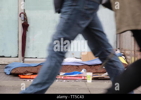 Le persone camminare davanti a un senzatetto posto all'ingresso di un chiuso store Foto Stock