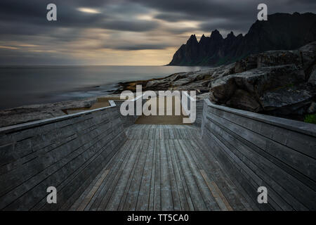 Passerella su Tugeneset costa rocciosa con le montagne sullo sfondo al tramonto, Norvegia Foto Stock