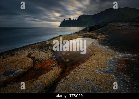 Tugeneset costa rocciosa con le montagne sullo sfondo al tramonto, Norvegia Foto Stock