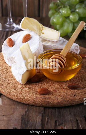 Formaggio Camembert su carta, uva, noci e miele nella ciotola di vetro sul bordo di taglio su sfondo di legno Foto Stock