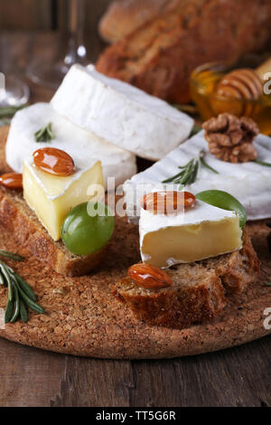 Formaggio Camembert su carta, uva, noci e miele nella ciotola di vetro sul bordo di taglio su sfondo di legno Foto Stock