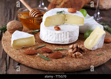 Formaggio Camembert su carta, uva, noci e miele nella ciotola di vetro sul bordo di taglio su sfondo di legno Foto Stock