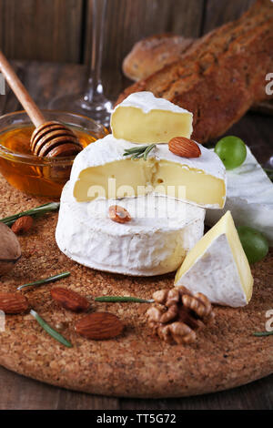 Formaggio Camembert su carta, uva, noci e miele nella ciotola di vetro sul bordo di taglio su sfondo di legno Foto Stock