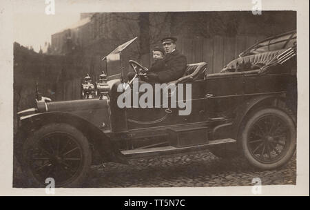 Vintage Edwardian Cartolina fotografica di un autista britannica, i giovani della scuola un ragazzo e un gatto in sella a un motorino classico auto. Presa nel dicembre 1909. Foto Stock