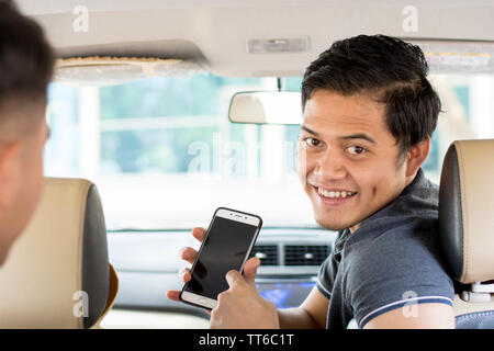 Online taxi driver, il trasporto, il concetto di viaggio - attraente uomo asiatico sorridente in Telecamera che mostra lo schermo dello smartphone per pagare e dare directio Foto Stock
