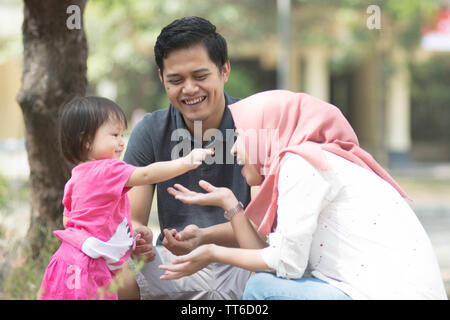 Felice giovani musulmani famiglia con uno dei bambini che giocano al parco con bambina mostrando qualcosa da sua mamma a giornata di sole Foto Stock