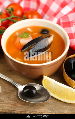 Una gustosa zuppa di gamberetti, cozze, pomodorini e olive nere in vaso su sfondo di legno Foto Stock