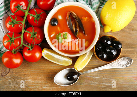 Una gustosa zuppa di gamberetti, cozze, pomodorini e olive nere in vaso su sfondo di legno Foto Stock