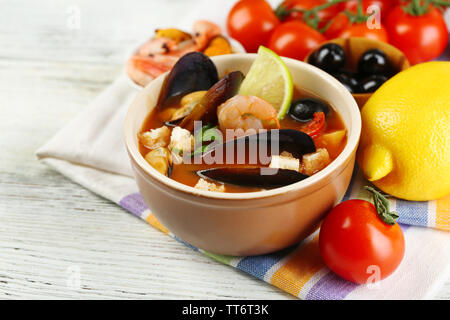 Una gustosa zuppa di gamberetti, cozze, pomodorini e olive nere in vaso su sfondo di legno Foto Stock