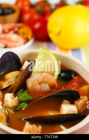 Una gustosa zuppa di gamberetti, cozze, pomodorini e olive nere in vaso su sfondo di legno Foto Stock