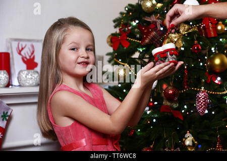 Bambina tenendo rosso scarpe poco vicino albero di Natale sul muro bianco sullo sfondo Foto Stock