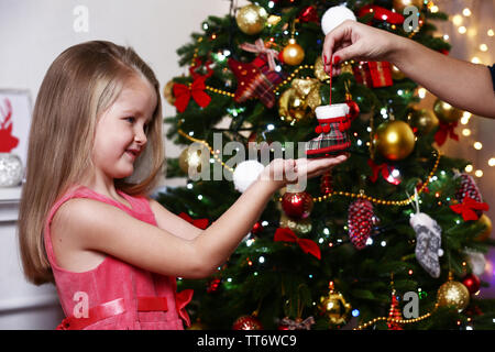 Bambina tenendo rosso scarpe poco vicino albero di Natale sul muro bianco sullo sfondo Foto Stock