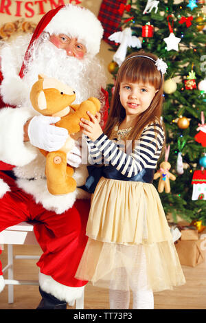 Babbo Natale dando presente a poco ragazza carina vicino albero di Natale a casa Foto Stock