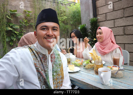 Il Portrait di uomo musulmano guardando la fotocamera mentre altri pople mangiare durante il ramadan celebrazione, rompere il digiuno Foto Stock