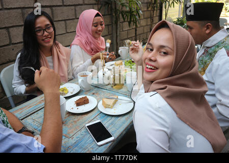 Il Portrait di giovani musulmani donna che guarda la fotocamera mentre altri pople mangiare durante il ramadan celebrazione, rompere il digiuno Foto Stock