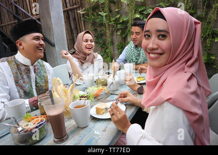 Il Portrait di giovani musulmani donna che guarda la fotocamera mentre altri pople mangiare durante il ramadan celebrazione, rompere il digiuno Foto Stock