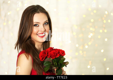 Ragazza sorridente con bouquet di rose rosse su sfondo luci Foto Stock