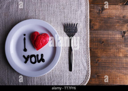 Cookie a forma di cuore sulla piastra con iscrizione ti amo, sul tovagliolo e tavolo in legno sfondo Foto Stock