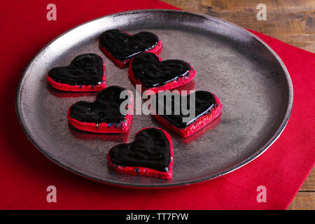 I cookie in forma di cuore ricoperte di cioccolato sul vassoio di metallo con il tovagliolo sulla tavola di legno sfondo Foto Stock