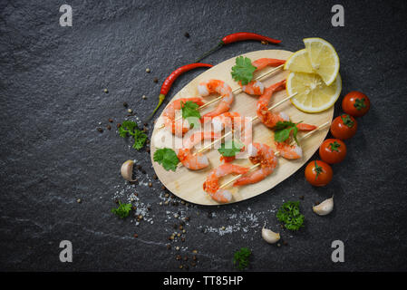 Gamberi spiedini cucinati di frutti di mare con salsa di erbe e spezie su uno sfondo di legno / Close up crostacei di gamberi cotti Foto Stock