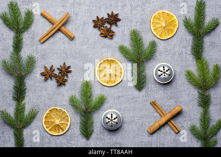 Natale partita di tris deco con secchi Arance, aniseeds, cinamon bastoni, Abete rami e campane di argento su sfondo grigio Foto Stock