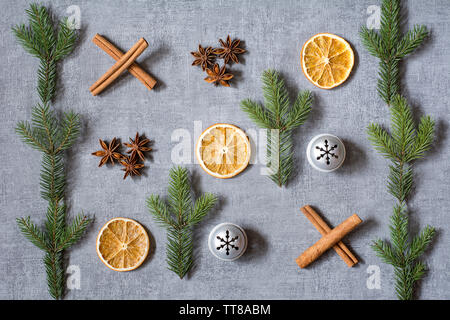 Natale partita di tris deco con secchi Arance, aniseeds, cinamon bastoni, Abete rami e campane di argento su sfondo grigio Foto Stock