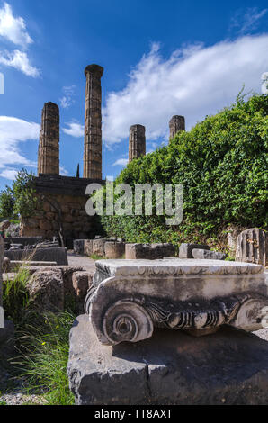 Delphi, Phocis / Grecia. Tempio di Apollo e un ordine ionico capitale di un antico colonna presso il sito archeologico di Delfi. Giornata di sole, cielo molto nuvoloso Foto Stock