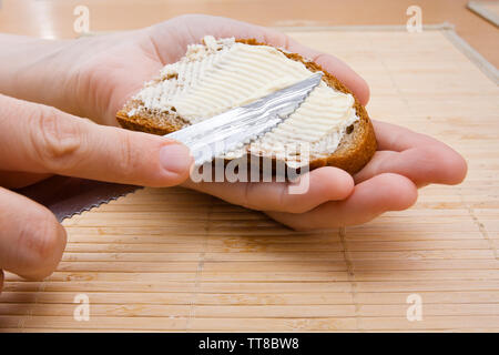 Donna mani diffusione di burro sul pezzo di pane di segale, primo piano Foto Stock