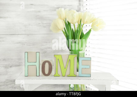 Home in lettere colorate e fiori di primavera in luce interno bianco Foto Stock