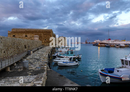 Heraklion, Creta - Grecia. La fortezza di Koules (Castello a Mare) al vecchio porto veneziano nella città di Heraklion. Tradizionale colorate barche da pesca Foto Stock