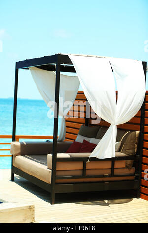 Un comodo divano vicino alla piscina del resort oltre il cielo blu sullo sfondo Foto Stock