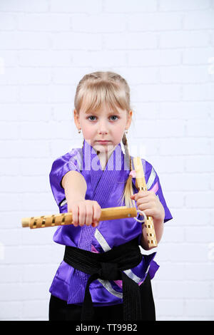 Bambina in kimono facendo esercizi con nunchaku su sfondo a parete Foto Stock