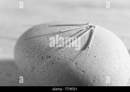 Aghi di agopuntura su spa pietra sul tavolo di legno, primo piano Foto Stock