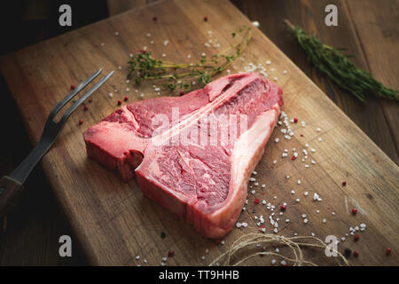 Materie t bone steak di carni bovine sul banco del macellaio con pepe, sale, erbe, chiudere lo spago Foto Stock