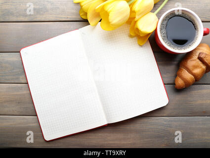 Tazza di caffè con croissant freschi, tulipani e foglio di carta bianco su sfondo di legno Foto Stock