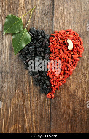 Goji bacche e uvetta disposti in forma di cuore su sfondo di legno Foto Stock