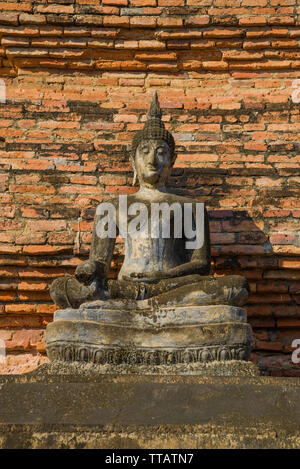 La scultura antica di un Buddha seduto contro un muro di mattoni. Frammento di antico tempio buddista Wat Mahathat. Sukhothai, Thailandia Foto Stock