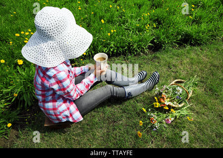 Giovane donna con tazza di caffè seduti sul prato all'aperto Foto Stock