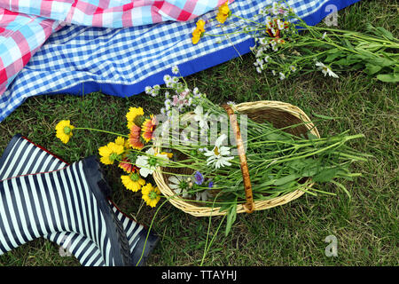 Bella composizione con bouquet di fiori selvatici e stivali di gomma sul prato all'aperto Foto Stock