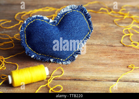 Cuore del denim e filettatura su sfondo di legno Foto Stock