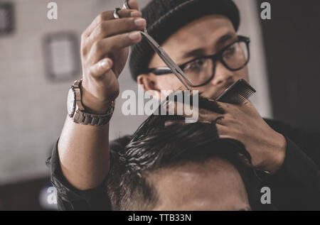 Close up ritratto professionale di barbiere rendendo il taglio di capelli del suo uomo attraente costumista con forbici e pettine barbiere vintage Foto Stock