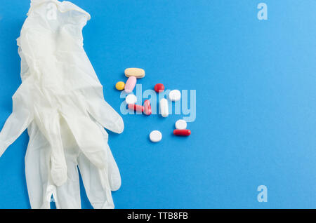 Guanti medici colorate di bianco compresse e pillole su sfondo blu closeup Foto Stock