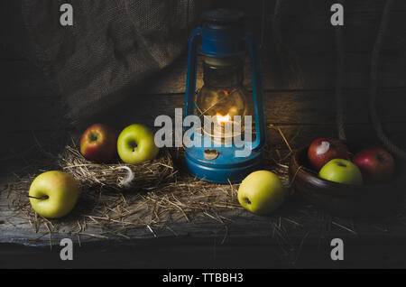 Le mele nel fieno accesa una lampada di kerosene sullo sfondo di vecchie schede madri e tela Foto Stock