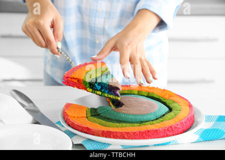 Giovane donna di taglio torta arcobaleno in cucina Foto Stock