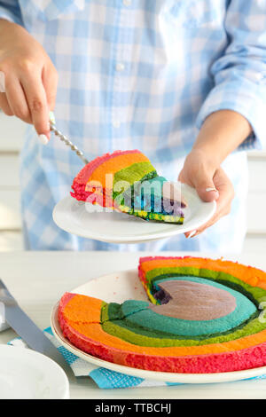 Giovane donna di taglio torta arcobaleno in cucina Foto Stock